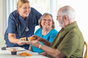 femmina medico o infermiera servendo anziano adulto coppia panini a tavolo foto