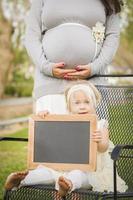 incinta mamma dietro a bambino ragazza nel sedia Tenere vuoto lavagna foto