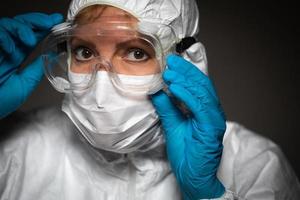 femmina medico lavoratore indossare protettivo viso maschera e Ingranaggio contro buio sfondo foto