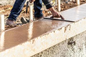 costruzione lavoratore utilizzando legna cazzuola su bagnato cemento formatura cimasa in giro nuovo piscina foto