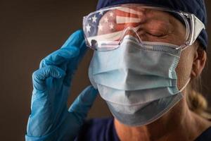 americano bandiera riflettendo su afflitto femmina medico lavoratore indossare protettivo viso maschera e occhiali foto