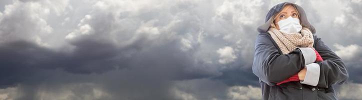 donna indossare medico viso maschera e giacca nel nuvoloso tempestoso tempo metereologico bandiera foto