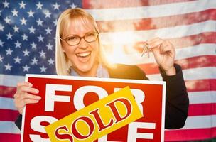 giovane donna Tenere Casa chiavi e venduto cartello nel davanti di americano bandiera foto
