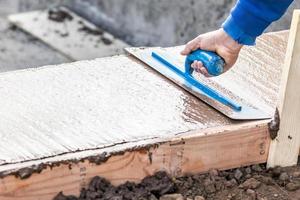 costruzione lavoratore utilizzando cazzuola su bagnato cemento formatura cimasa in giro nuovo piscina foto