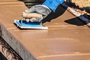 costruzione lavoratore utilizzando mano scanalatore su bagnato cemento formatura cimasa in giro nuovo piscina foto