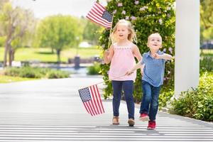 giovane sorella e fratello agitando americano bandiere a il parco foto