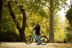 bel giovane con bicicletta elettrica nel parco autunnale foto