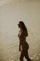 giovane donna nel bikini a piedi di il mare su un' tramonto di estate giorno foto