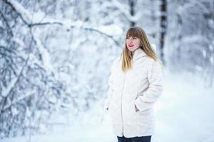 bellissimo sorridente fiducioso giovane bianca donna bella viso con luminosa rosso labbra nel bianca pelliccia cappotto guardare a telecamera in posa solo a nevoso foresta foto