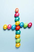 Pasqua creativo composizione. colorato lucido Pasqua uova di cui su nel forma di attraversare su leggero blu pastello sfondo. foto