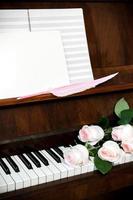 pianoforte, pallido rosa Rose su tastiera del computer, musica carta e bianca vuoto con rosa penna d'oca penna. foto