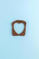 uno segale pane fetta con lavorato buco di cuore forma nel esso su leggero blu sfondo. creativo minimo concetto. foto