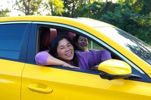 Due asiatico donne siamo gli amici. sorridente felicemente, essi guardato attraverso il autisti finestra di un' giallo macchina. mentre in viaggio insieme su fine settimana. morbido e selettivo messa a fuoco. foto