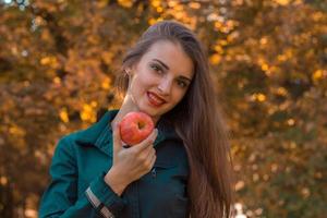 giovane bellissimo ragazza con lungo capelli detiene un Mela nel il suo mano e sorridente avvicinamento foto