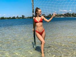 bellissimo giovane donna nel rosso nuotare completo da uomo in posa e guardare lontano vicino spiaggia pallavolo netto foto