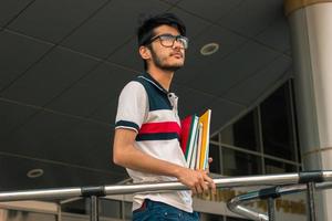 giovane alunno ragazzo con libri nel mani indossa un' bicchieri e guardare lontano foto