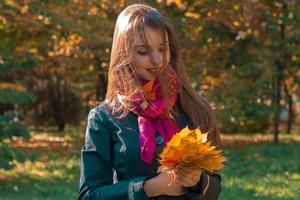 giovane ragazza nel rosa sciarpa mantiene le foglie nel il mani di il parco foto