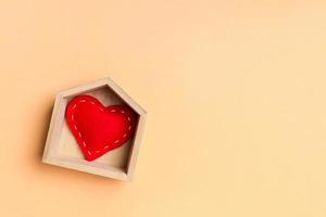 superiore Visualizza di rosso tessile cuore nel un' di legno Casa su colorato sfondo. casa dolce casa concetto. San Valentino giorno foto