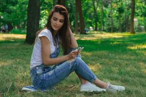 sorridente donna seduta su il erba e ascolta per il cuffie musica foto