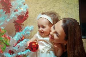 Natale umore. madre decora il Natale albero con il suo poco figlia per il primo tempo foto
