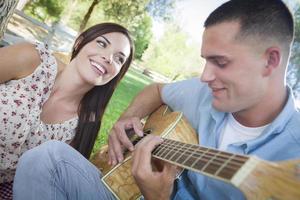 misto gara coppia a il parco giocando chitarra e cantando foto