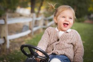 giovane bambino piccolo ridendo e giocando su giocattolo trattore al di fuori foto