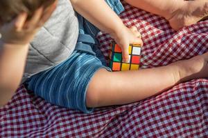 bambino ragazzo seduta su picnic coperta giocando con cubo puzzle foto