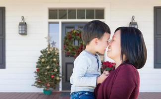 Cinese madre e misto gara bambino sfregamento nasi in piedi su Natale decorato davanti veranda foto