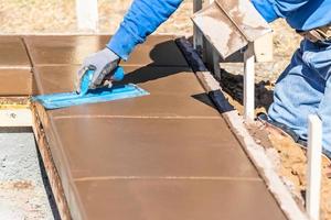 costruzione lavoratore utilizzando cazzuola su bagnato cemento formatura cimasa in giro nuovo piscina foto