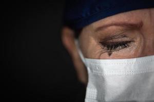 lacrimoso stressato femmina medico o infermiera indossare medico viso maschera su buio sfondo foto