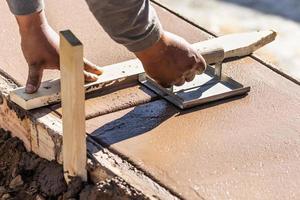 costruzione lavoratore utilizzando mano scanalatore su bagnato cemento formatura cimasa in giro nuovo piscina foto