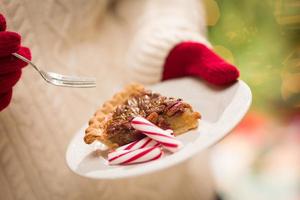 donna indossare rosso guanti Tenere piatto di pecan torta con menta piperita caramella contro decorato albero e luci foto