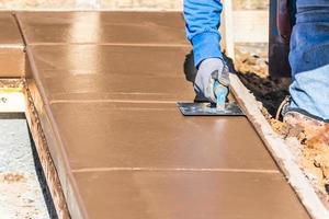 costruzione lavoratore utilizzando mano scanalatore su bagnato cemento formatura cimasa in giro nuovo piscina foto