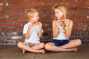 carino giovane cuacasian ragazzo e ragazza mangiare anguria contro mattone parete foto