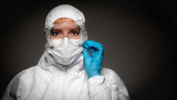 femmina medico lavoratore indossare protettivo viso maschera e Ingranaggio contro buio sfondo foto