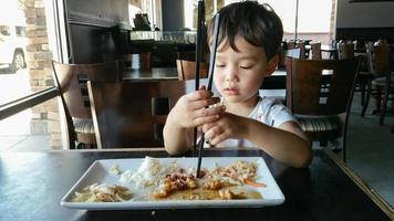 carino giovane Cinese e caucasico ragazzo apprendimento per uso bastoncini a ristorante foto