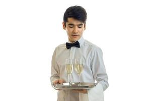 simpatico giovane Cameriere abbassato il suo occhi giù e Tenere un' vassoio con Due bicchieri di vino foto