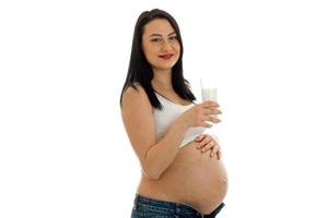 brunetta incinta futuro madre bevande latte e guardare a il telecamera isolato su bianca sfondo foto