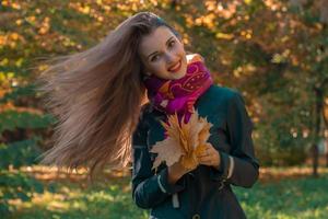 bellissimo ragazza con lungo capelli chi volare su il vento mantiene il le foglie nel loro mani e sorrisi foto