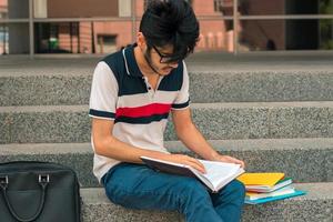 un' giovane uomo seduta su il strada e legge libri foto