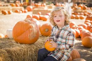 poco ragazzo seduta e Tenere il suo zucca a zucca toppa foto