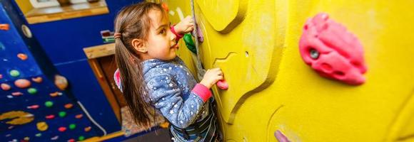 poco bambino ragazza con divertente sentire stile arrampicata verticale parete e uomo belaying sua a partire dal sotto foto