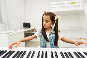 carino poco ragazza giochi su pianoforte, sintetizzatore. addestramento. formazione scolastica. scuola. estetico addestramento. elementare aula. foto