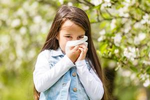 poco ragazza è soffiaggio sua naso vicino primavera albero nel fioritura foto