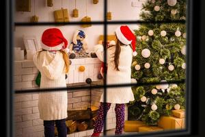 Due ragazze nel davanti di Natale albero con i regali e fuoco posto attraverso il finestra foto