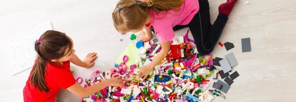 bambini giocare con un' giocattolo progettista su il pavimento di il figli di camera. Due bambini giocando con colorato blocchi. scuola materna educativo Giochi. vicino su Visualizza. foto