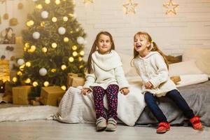 Due ragazze nel davanti di Natale albero con i regali e fuoco posto foto