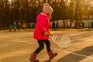 poco ragazza apprendimento per colpire il tennis sfera. poco ragazza tennis giocatore con palla e racchetta su Tribunale. attivo esercizio per bambini foto