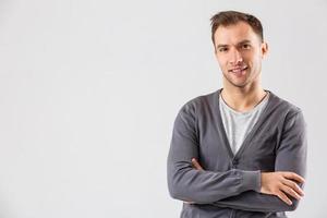 casualmente bello. fiducioso giovane bello uomo conservazione braccia attraversato e sorridente mentre in piedi contro bianca sfondo foto