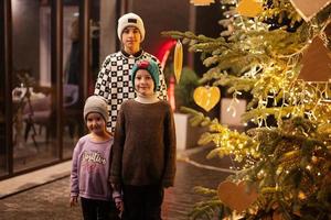 tre bambini avendo divertimento vicino illuminato Natale albero all'aperto nel sera. foto